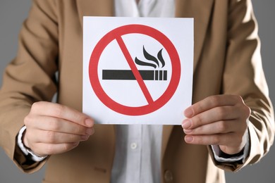 Woman holding card with no smoking sign on gray background, closeup