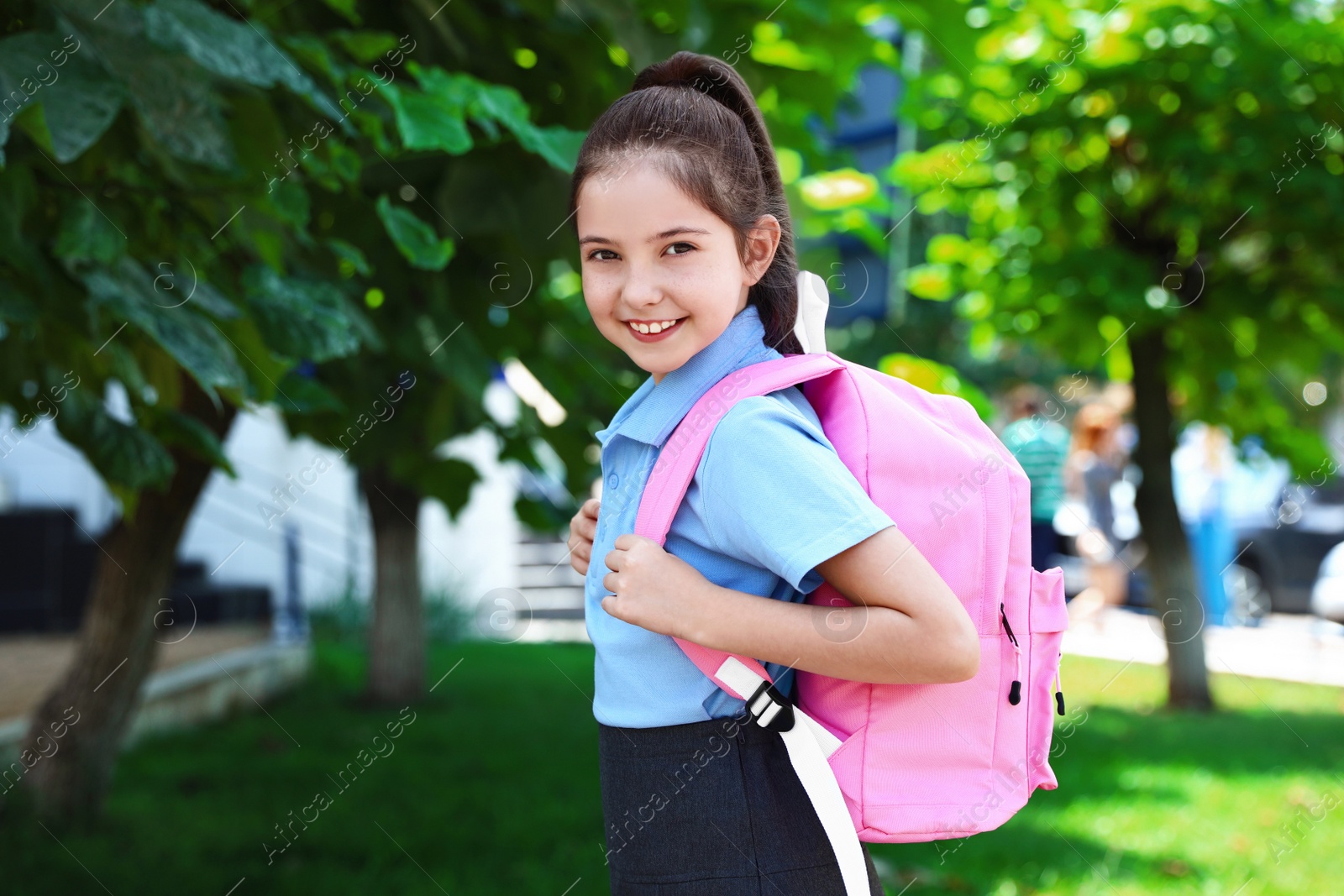 Photo of Cute little girl in school uniform with pink backpack on street