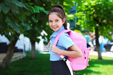 Photo of Cute little girl in school uniform with pink backpack on street