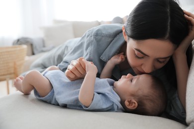 Photo of Young woman with her cute baby on sofa at home