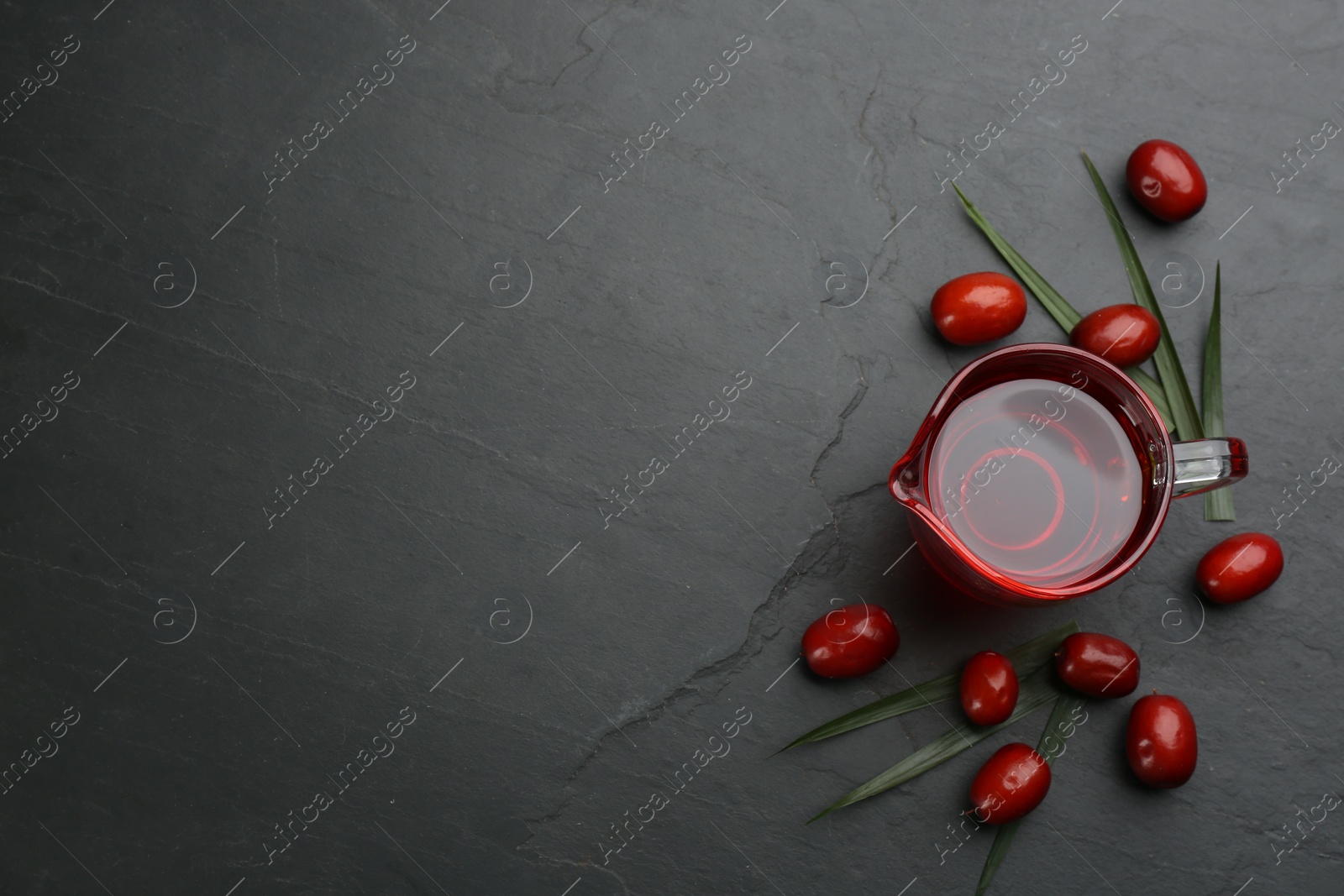 Photo of Palm oil in glass jug, tropical leaf and fruits on black table, flat lay. Space for text