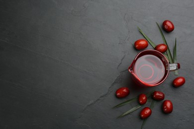 Photo of Palm oil in glass jug, tropical leaf and fruits on black table, flat lay. Space for text