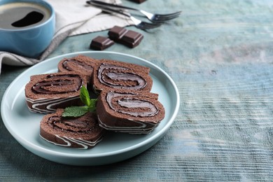 Tasty chocolate cake roll with cream and mint on blue wooden table, space for text