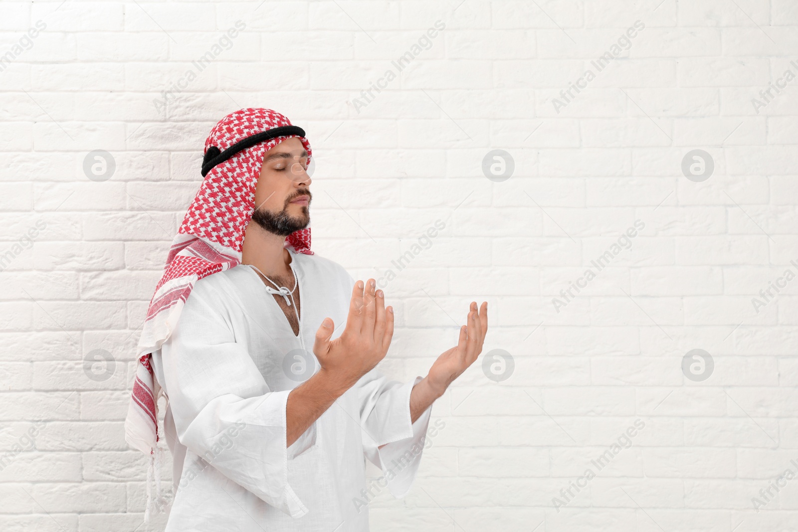 Photo of Muslim man praying near brick wall. Space for text