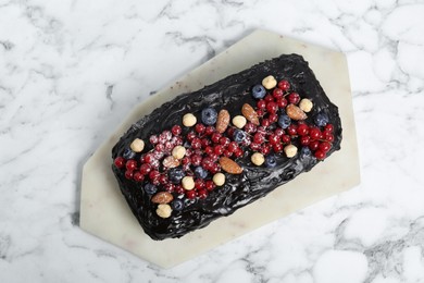 Photo of Delicious chocolate sponge cake with berries and nuts on white marble table, top view