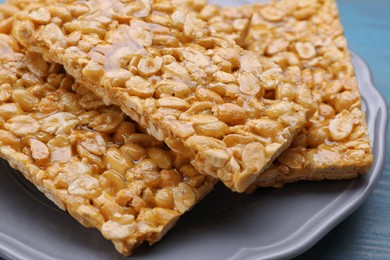 Photo of Delicious peanut bars (kozinaki) on light blue wooden table, closeup