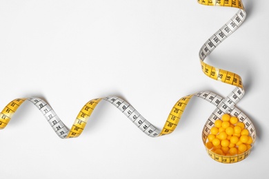 Weight loss pills and measuring tape on white background