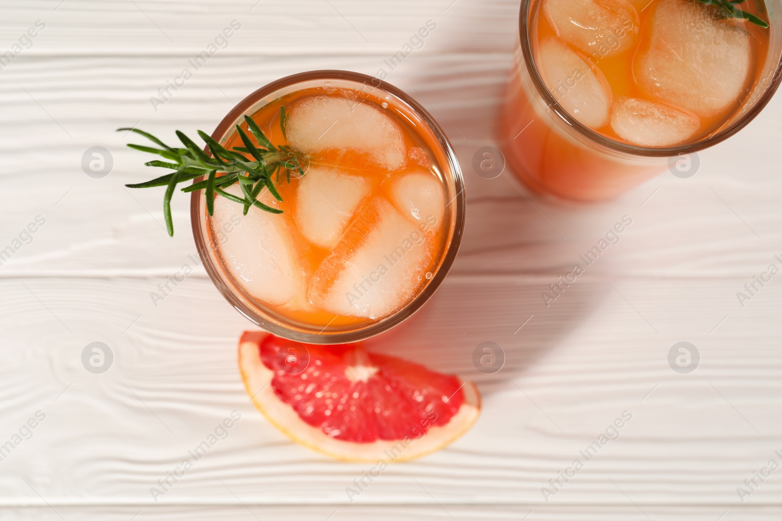 Photo of Tasty grapefruit drink with ice and rosemary in glasses on white wooden table, top view