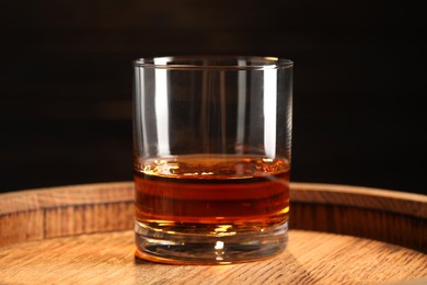 Photo of Glass of tasty whiskey on wooden barrel, closeup