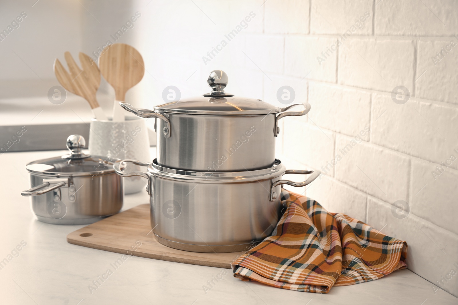 Photo of Set of stainless steel cookware and kitchen utensils on table near white brick wall