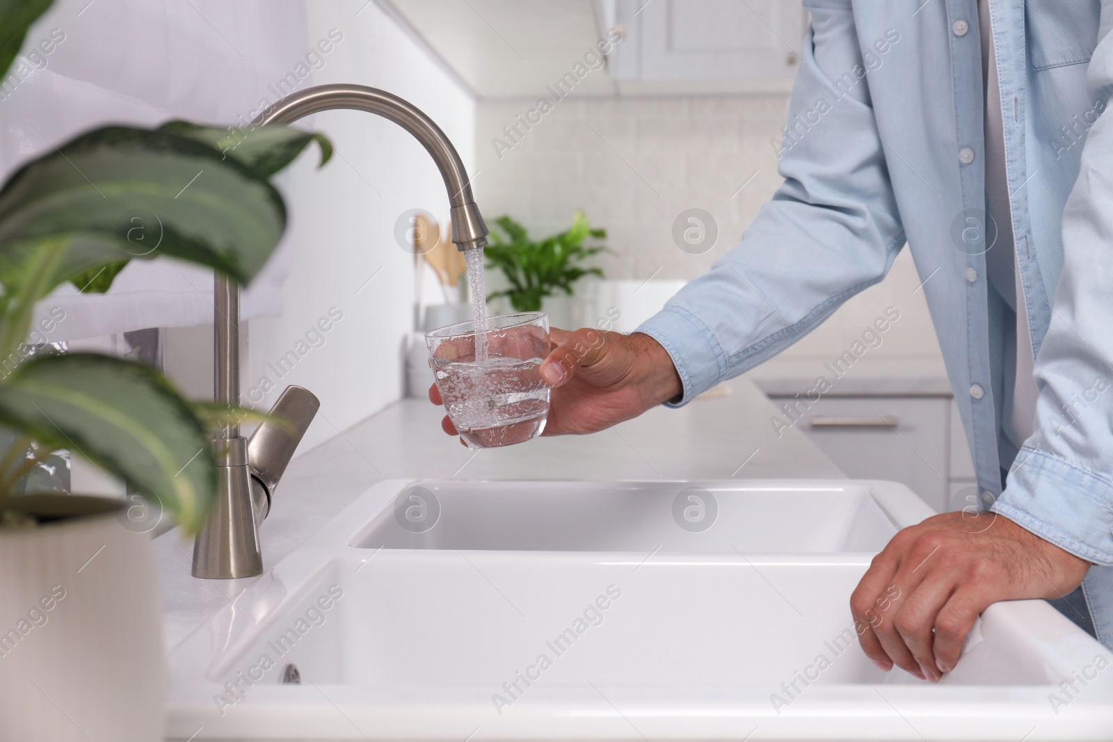 Photo of Man filling glass with water from tap in kitchen, closeup