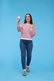 Photo of Smiling young woman taking selfie with smartphone on light blue background