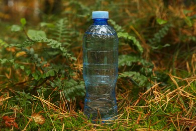 Photo of Plastic bottle of fresh water on ground in forest