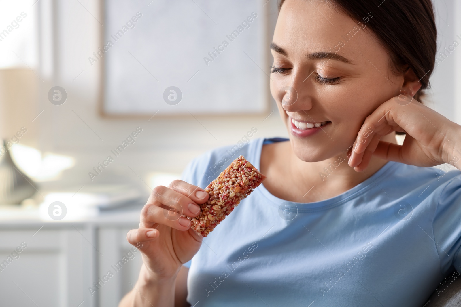 Photo of Woman holding tasty granola bar at home