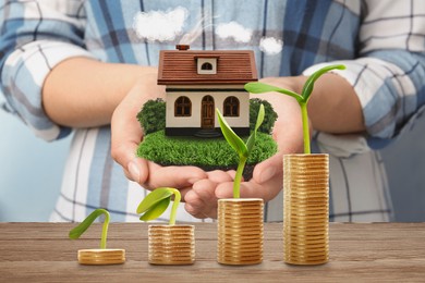 Stack of coins on wooden table and woman holding house model. Real estate investing