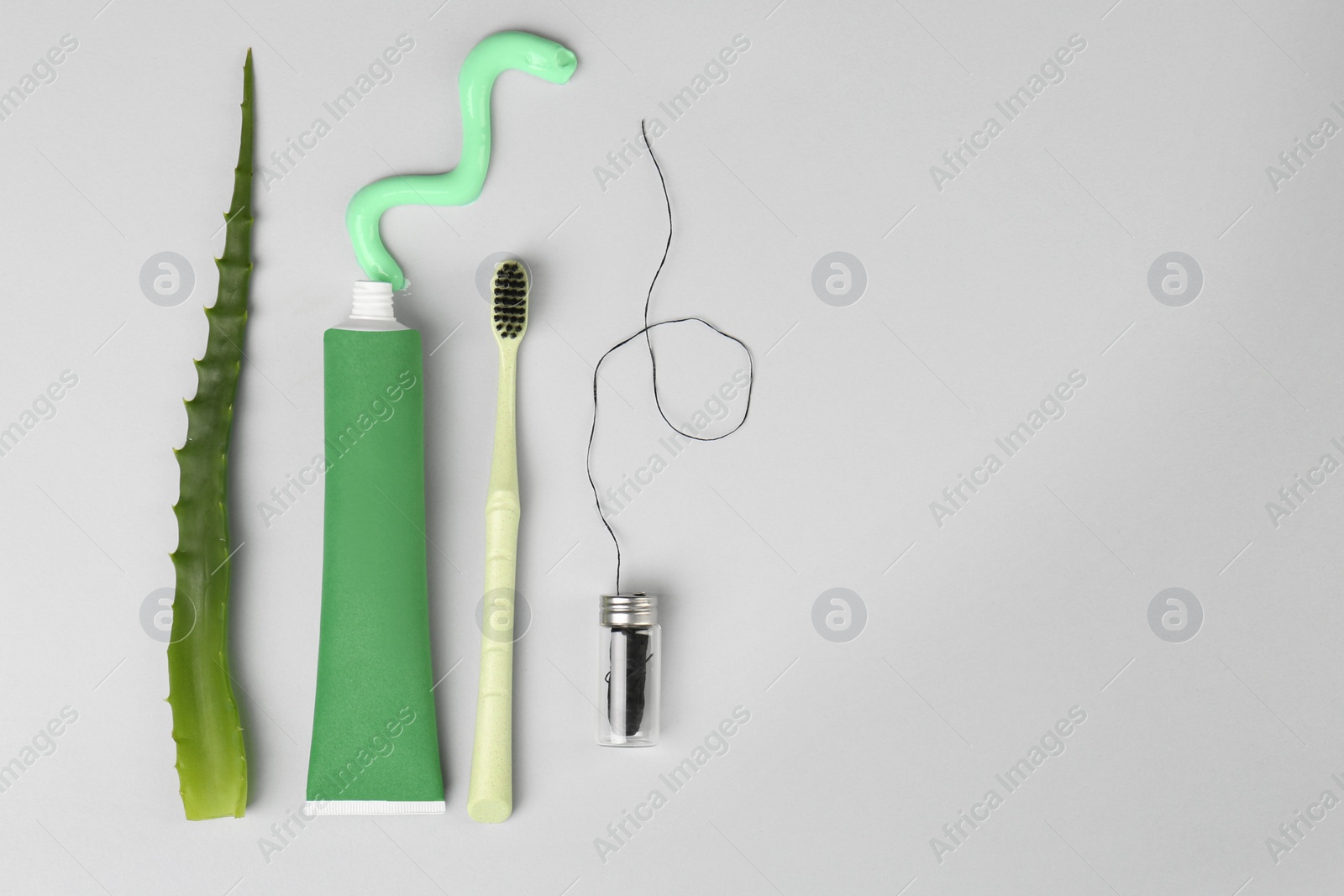 Photo of Tube of toothpaste, toothbrush, dental floss and fresh aloe on light grey background, flat lay. Space for text