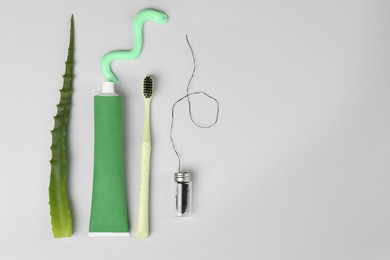 Tube of toothpaste, toothbrush, dental floss and fresh aloe on light grey background, flat lay. Space for text