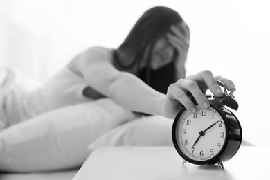 Image of Young woman turning off alarm clock at home in morning, selective focus. Black and white photography