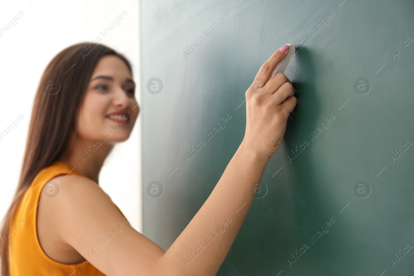 Photo of Young female teacher writing on blackboard in classroom