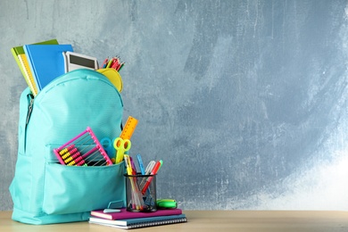 Bright backpack with school stationery on brown wooden table against blue background, space for text