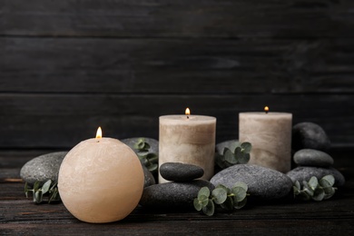 Photo of Composition with burning candles, spa stones and eucalyptus on dark wooden table