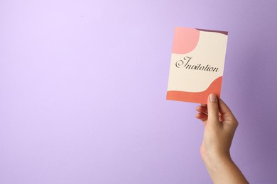 Woman holding beautiful card with word Invitation on lilac background, closeup. Space for text