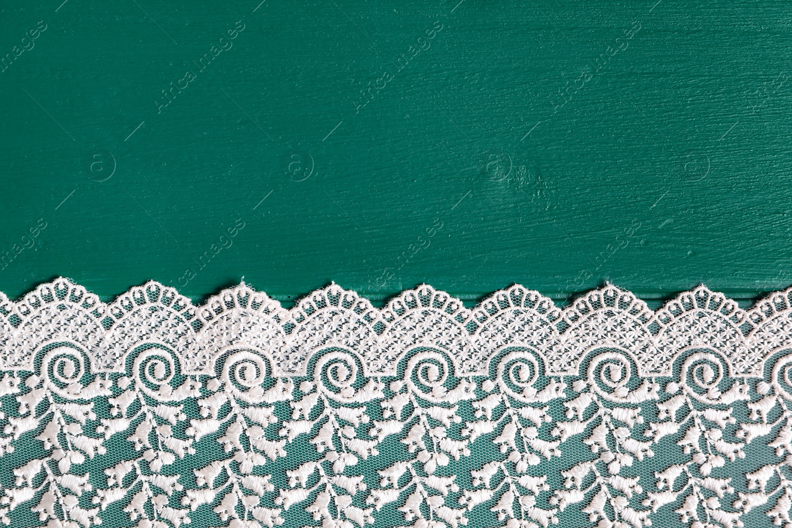 Photo of Beige lace on green wooden table, top view. Space for text