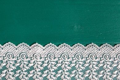 Photo of Beige lace on green wooden table, top view. Space for text