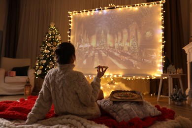 Photo of MYKOLAIV, UKRAINE - DECEMBER 24, 2020: Woman watching Harry Potter and Philosopher's Stone movie via video projector in room. Cozy winter holidays atmosphere
