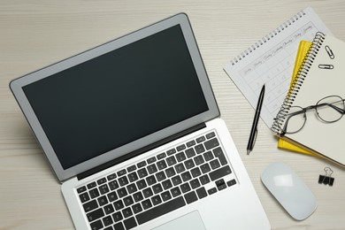 Modern laptop, glasses and office stationery on white wooden table, flat lay. Distance learning