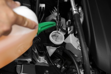 Photo of Man pouring liquid from plastic canister into car washer fluid reservoir, closeup