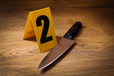 Photo of Bloody knife and crime scene marker on wooden table