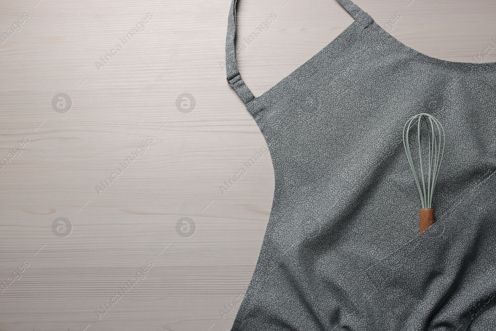 Photo of Stylish apron and whisk on white wooden table, top view. Mockup for design