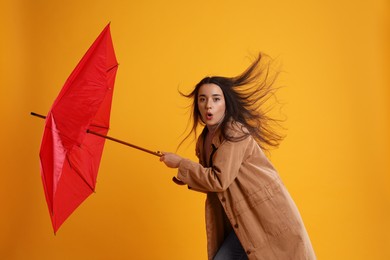Photo of Emotional woman with umbrella caught in gust of wind on yellow background