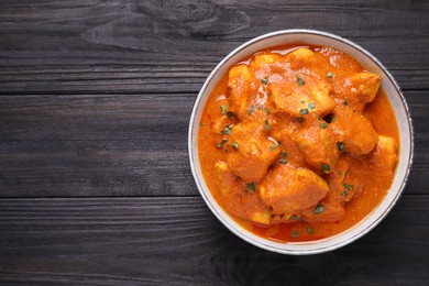 Photo of Bowl of delicious chicken curry on black wooden table, top view. Space for text