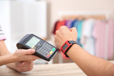 Man using terminal for contactless payment with smart watch in shop, closeup