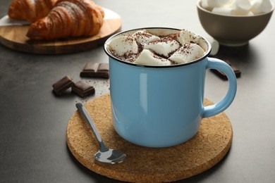 Delicious hot chocolate with marshmallows, cocoa powder and spoon on grey table, space for text