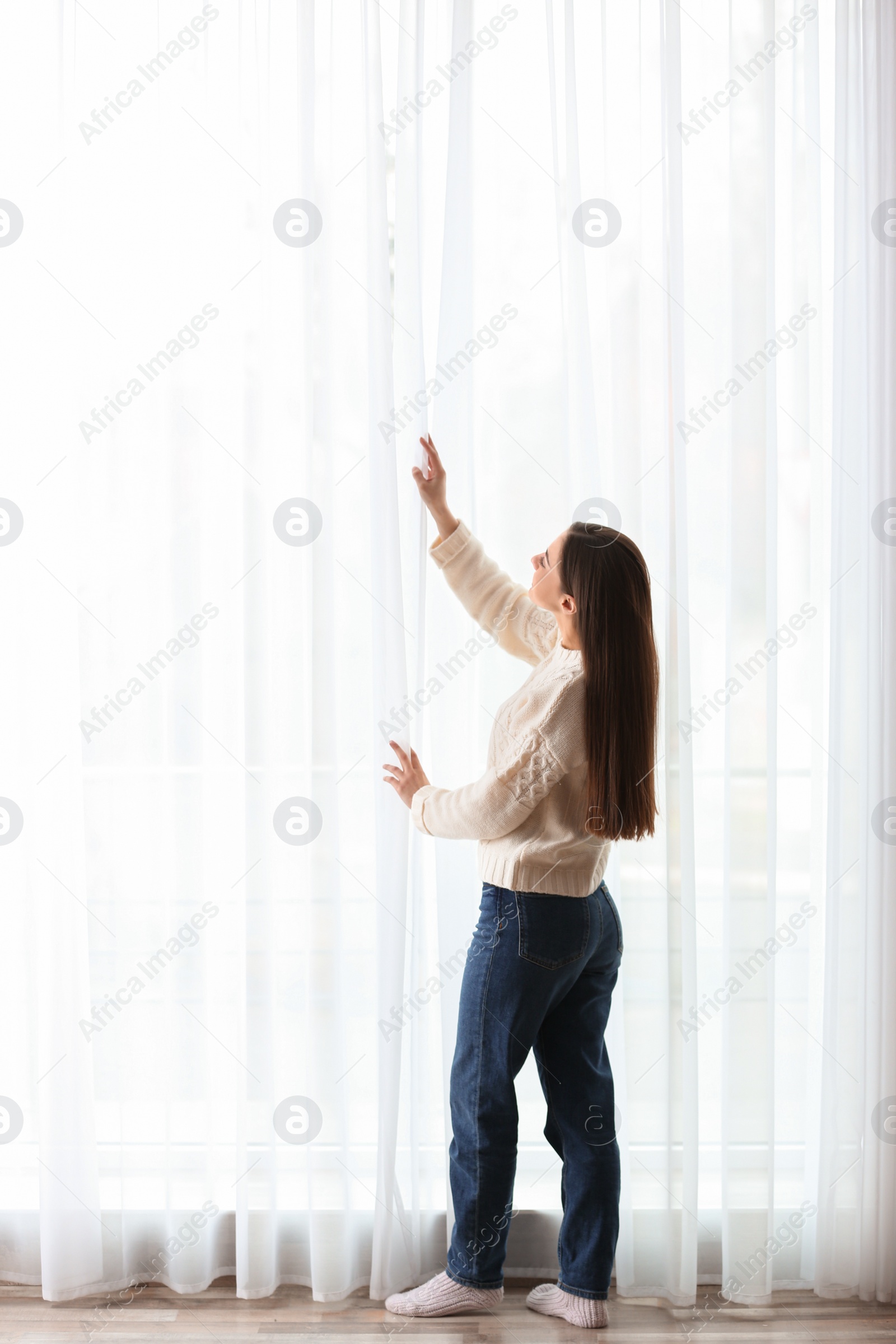 Photo of Young woman opening window curtains at home