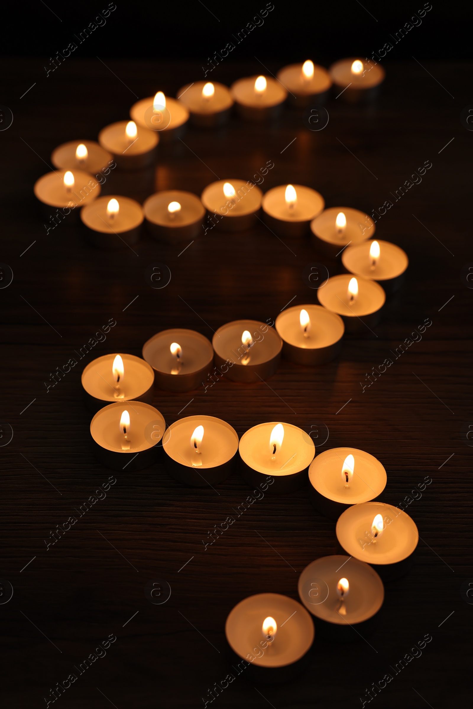 Photo of Burning candles on wooden table in darkness