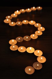 Photo of Burning candles on wooden table in darkness