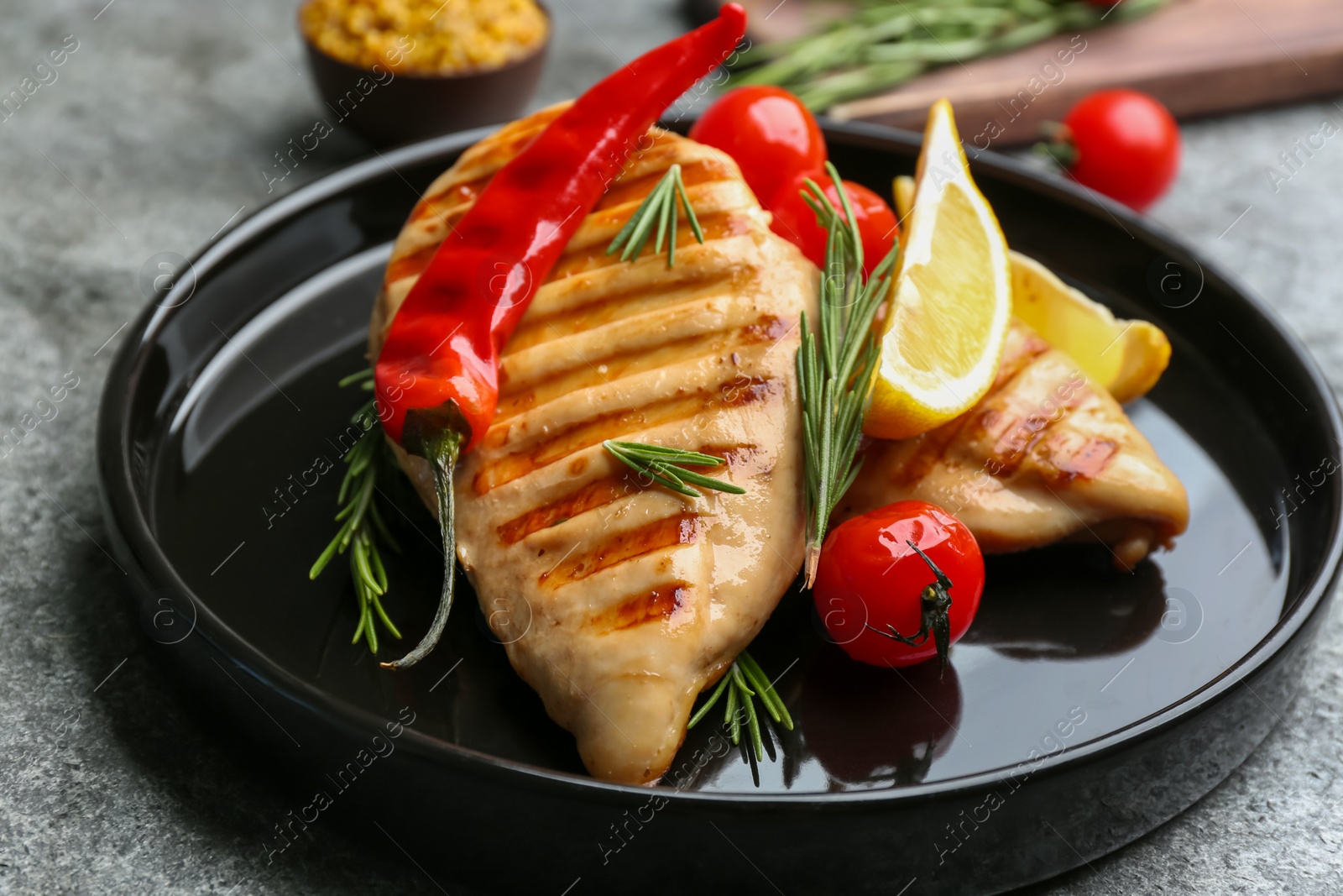 Photo of Tasty grilled chicken fillets with lemon, chili pepper and rosemary on grey table, closeup