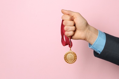 Man holding golden medal on color background, closeup. Space for text