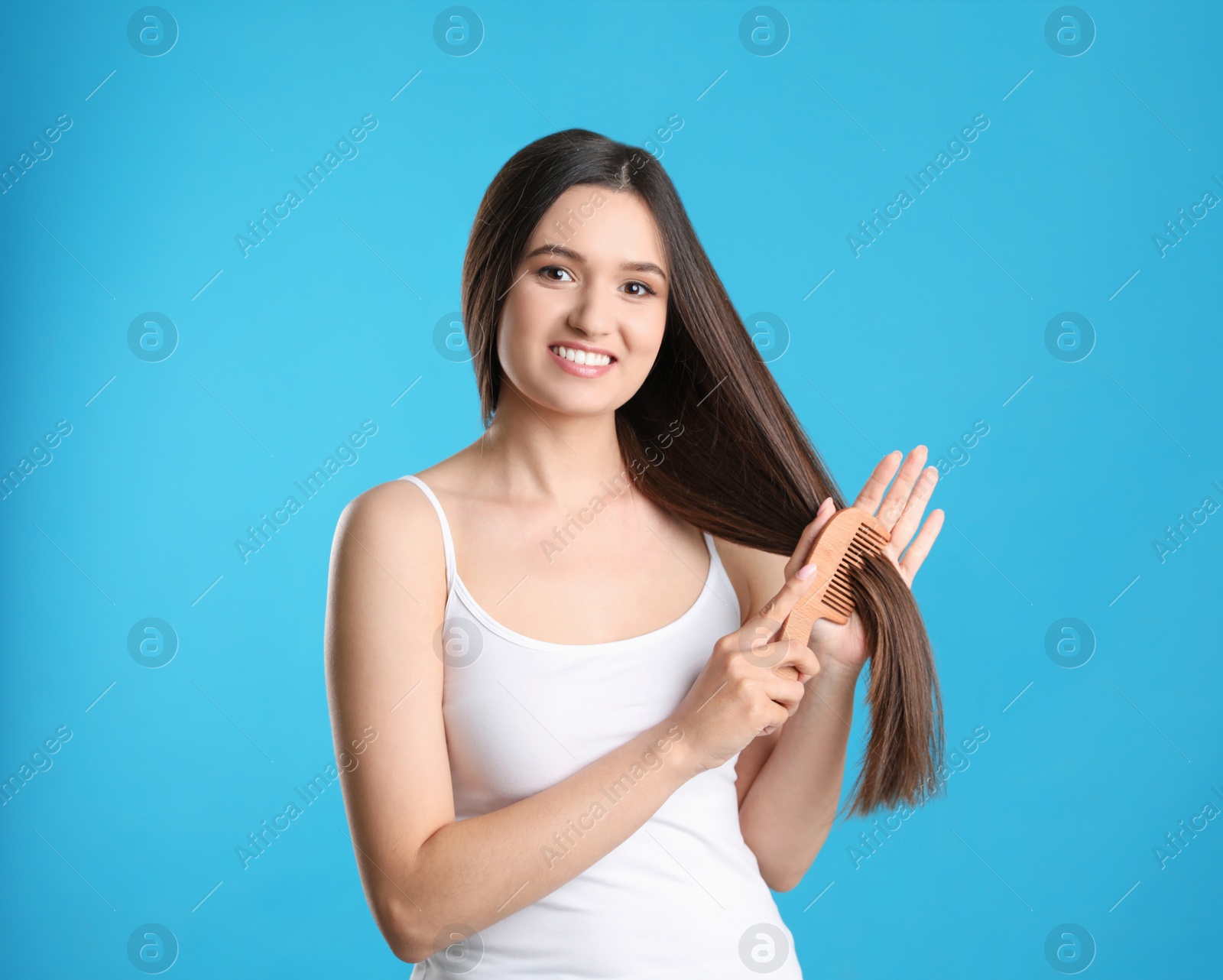 Photo of Beautiful smiling young woman with hair comb on color background