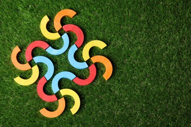 Photo of Colorful wooden pieces of play set on green grass, top view with space for text. Educational toy for motor skills development