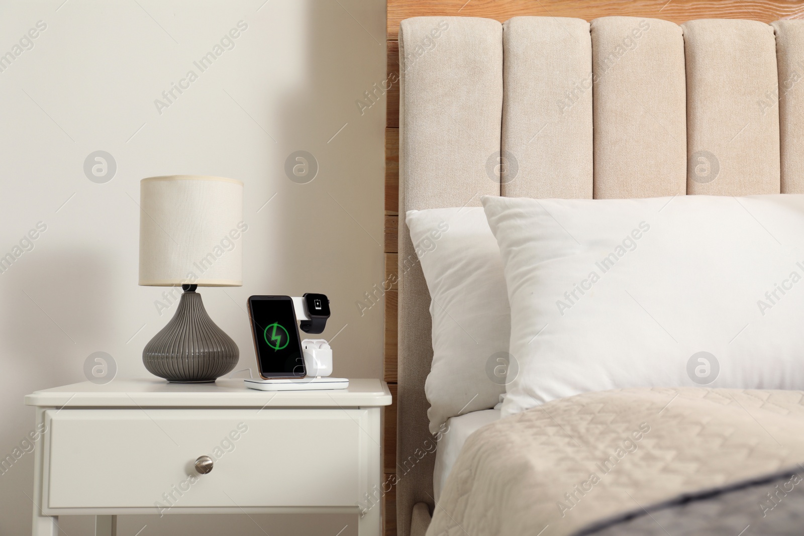 Photo of Different gadgets charging on wireless pad in bedroom