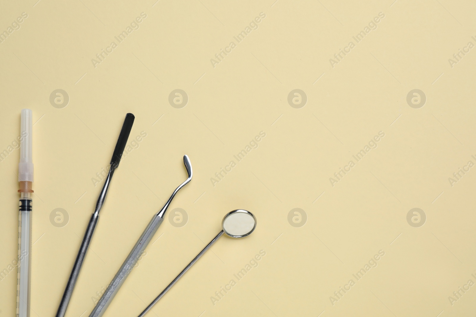 Photo of Set of dentist's tools and syringe on pale yellow background, flat lay. Space for text