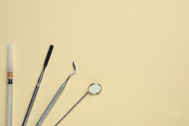 Set of dentist's tools and syringe on pale yellow background, flat lay. Space for text