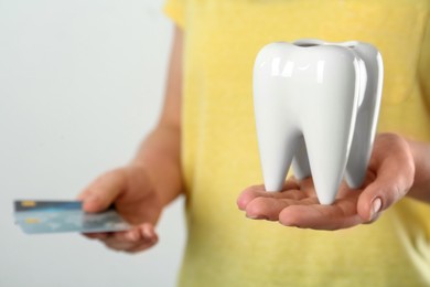 Photo of Woman holding ceramic model of tooth and credit cards on light background, closeup. Expensive treatment