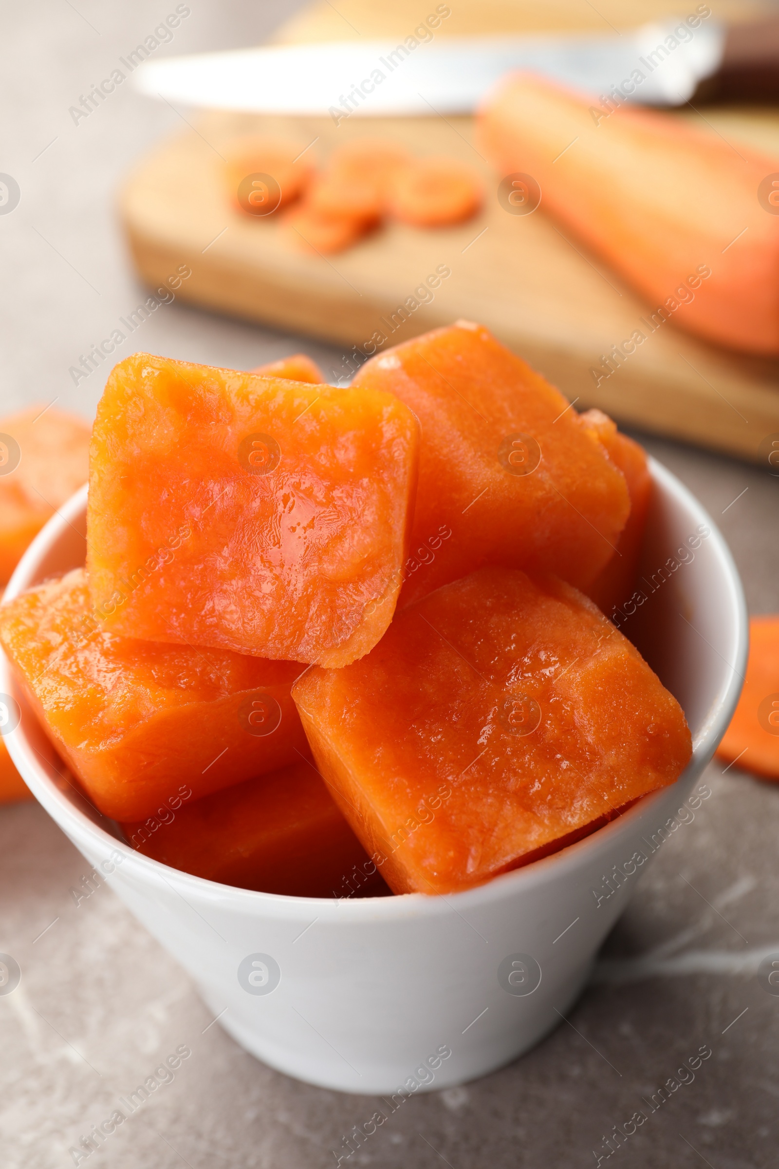 Photo of Bowl of frozen carrot puree cubes and ingredient on marble table, closeup