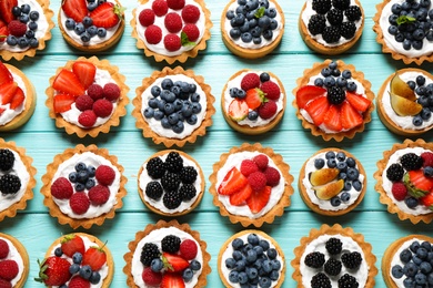 Many different berry tarts on blue wooden table, flat lay. Delicious pastries